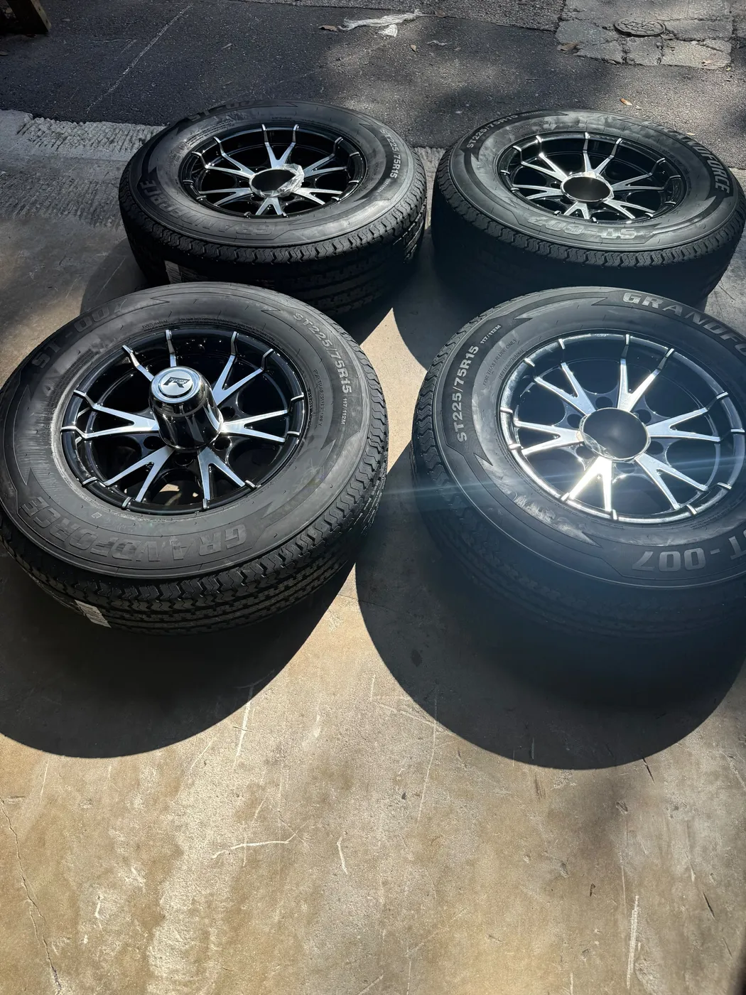 Four new ST225/75R15 trailer tires mounted on black machined aluminum wheels